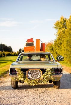 an old car with luggage on top parked in the middle of a gravel road next to trees