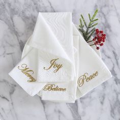 white towels with gold lettering on them sitting on a marble countertop next to a potted plant