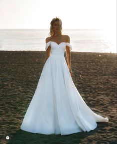 a woman standing on top of a sandy beach wearing a white dress and holding her hands in her pockets