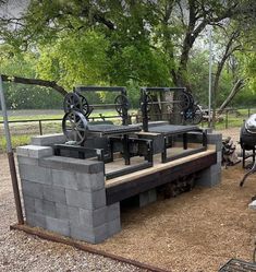 an outdoor grill made out of cinder blocks and steel wheels on the outside, sitting next to a fire pit