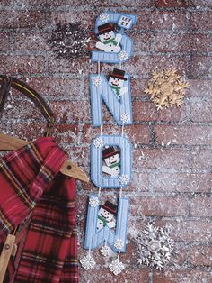 snowmen are hanging from clothes pins on a brick wall next to a sled