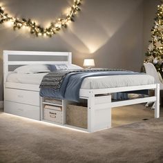 a white bed with drawers underneath it and christmas lights on the wall in the background