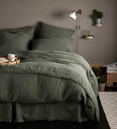 a bed with green linens in a bedroom next to a lamp and potted plant