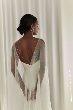 the back of a woman wearing a white dress with sheer sleeves and pearls on it