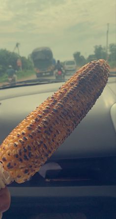 a person holding up a corn on the cob in front of a car window