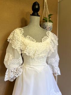 a white wedding dress on display in front of a wall with potted plant behind it