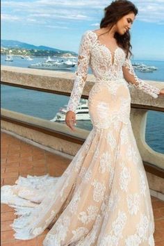 a woman in a long sleeved wedding dress standing on a balcony overlooking the ocean