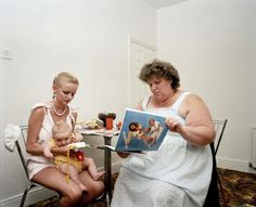 two women sitting at a table with a baby in her lap and an adult reading a book