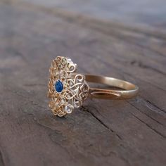 a gold ring with a blue stone in the middle sitting on a wooden table next to a pair of scissors