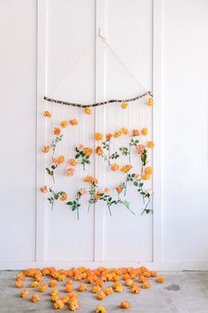 an arrangement of orange flowers is hanging on the wall next to some string and beads