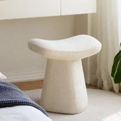 a white stool sitting on top of a bed next to a window