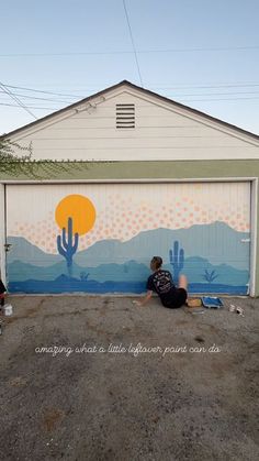 two people sitting on the ground in front of a garage door with a mural painted on it