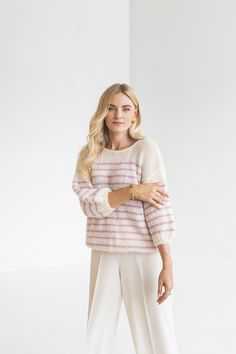 a woman standing in front of a white wall wearing a pink and white striped sweater