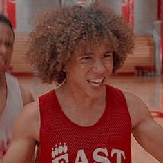 a young man in a red jersey is playing basketball while another person watches from the sidelines