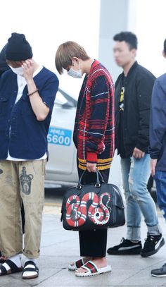 a group of young men standing next to each other on a sidewalk with one man covering his face