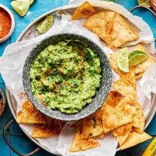 guacamole and tortilla chips on a plate with salsa in the background