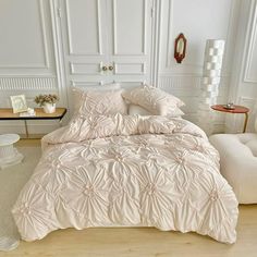 a bed with white comforter and pillows in a room next to a chair, side table and lamp