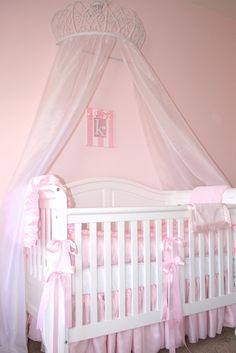 a baby's crib with pink bedding and a white canopy over it