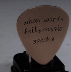 a guitar pick with words written on it sitting on top of a black stand that says when words fail, music speaks