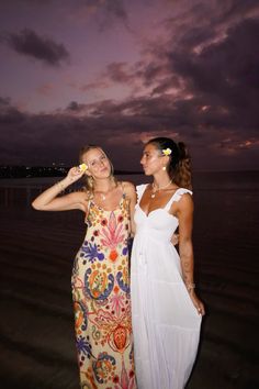 two women standing next to each other on a beach at night with the sky in the background