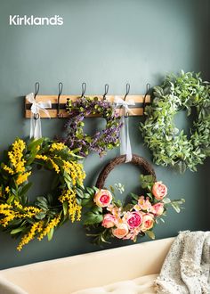 a wall with wreaths and flowers hanging on it's hooks, next to a bench