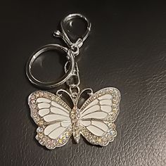 a white butterfly keychain sitting on top of a black surface with lots of crystals