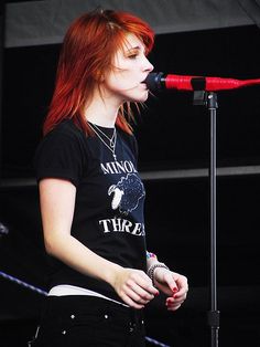 a woman with red hair standing in front of a microphone