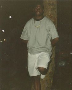 a man standing in front of a brick wall wearing white shorts and a t - shirt