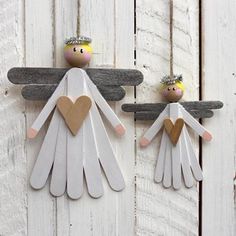 two wooden angel figurines hanging on a white painted wood plank wall with hearts in their hands