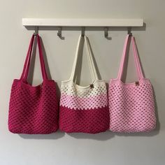 three pink and white bags hanging from hooks on the wall next to each other,