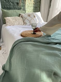 a person standing over a bed with green sheets and pillows on it, holding a straw hat