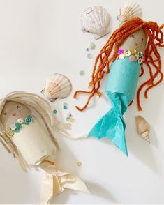 a doll with red hair laying on top of a table next to seashells