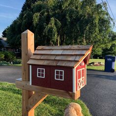 a brown teddy bear standing in front of a red and white house shaped mailbox