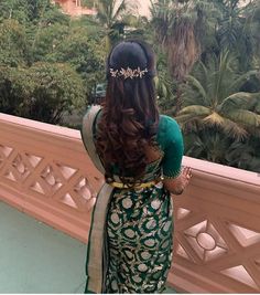 a woman with long hair wearing a green and gold sari standing on a balcony