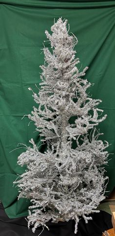 a silver tinsel christmas tree sitting on top of a wooden table next to a green curtain