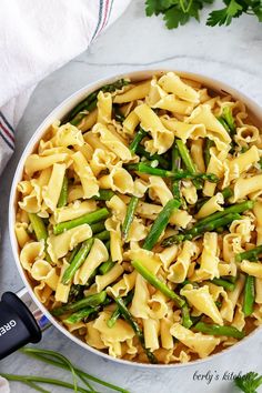 a bowl filled with pasta and asparagus on top of a white countertop