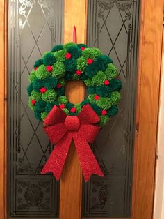 a green wreath with red bow hanging on the front door