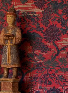 a wooden statue stands in front of a red wallpapered room with floral designs