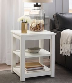 a white end table with a lamp on top and flowers in a vase next to it