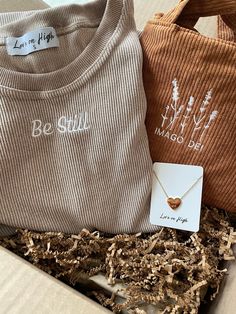 two sweaters and a necklace in a box with some wood chips on the floor