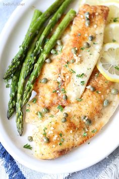 a white plate topped with chicken, asparagus and lemon wedges on top of a blue table cloth