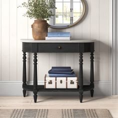 a black console table with books and a round mirror on the wall above it in a white room