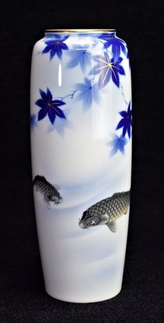 a white vase with blue flowers and fish on the bottom is shown in front of a black background