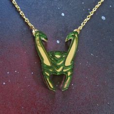 "Express your love for a charming shapeshifter when you wear this Loki God of Mischief Helmet Necklace! 💚 Loki Helmet Pendant is made from layered laser cut translucent green acrylic and mirrored gold acrylic. So shiny, you can see your reflection! 💚 Enchanting Helmet pendant measures 2\" from top to bottom and strung upon an 18\" golden chain with a large lobster clasp attachment. 💚 This fantasy necklace based on the Germanic Mythology of Thor comes on a super fun over sized card and wrapped Germanic Mythology, Loki Helmet, Loki God, God Of Mischief, Loki God Of Mischief, Fantasy Necklace, Necklace Green, The Avengers, Wooden Jewelry