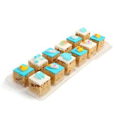 there are many pieces of cake in the tray on this white surface, with blue and yellow frosting