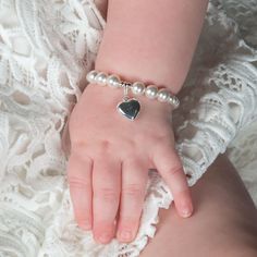 a baby's hand with a heart charm on it and pearls around the wrist