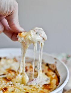 a person is dipping cheese into a casserole dish with melted cheese on top