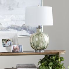 a table with a lamp and some pictures on it next to a potted plant