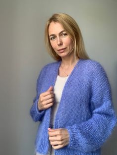 a woman wearing a blue cardigan standing in front of a wall with her hands on her hips