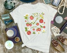 a white t - shirt with strawberries and daisies on it next to other items